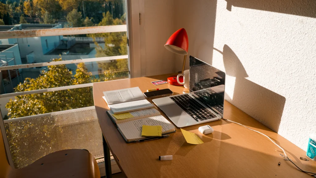 Desk with a laptop and notebooks by a window in natural light